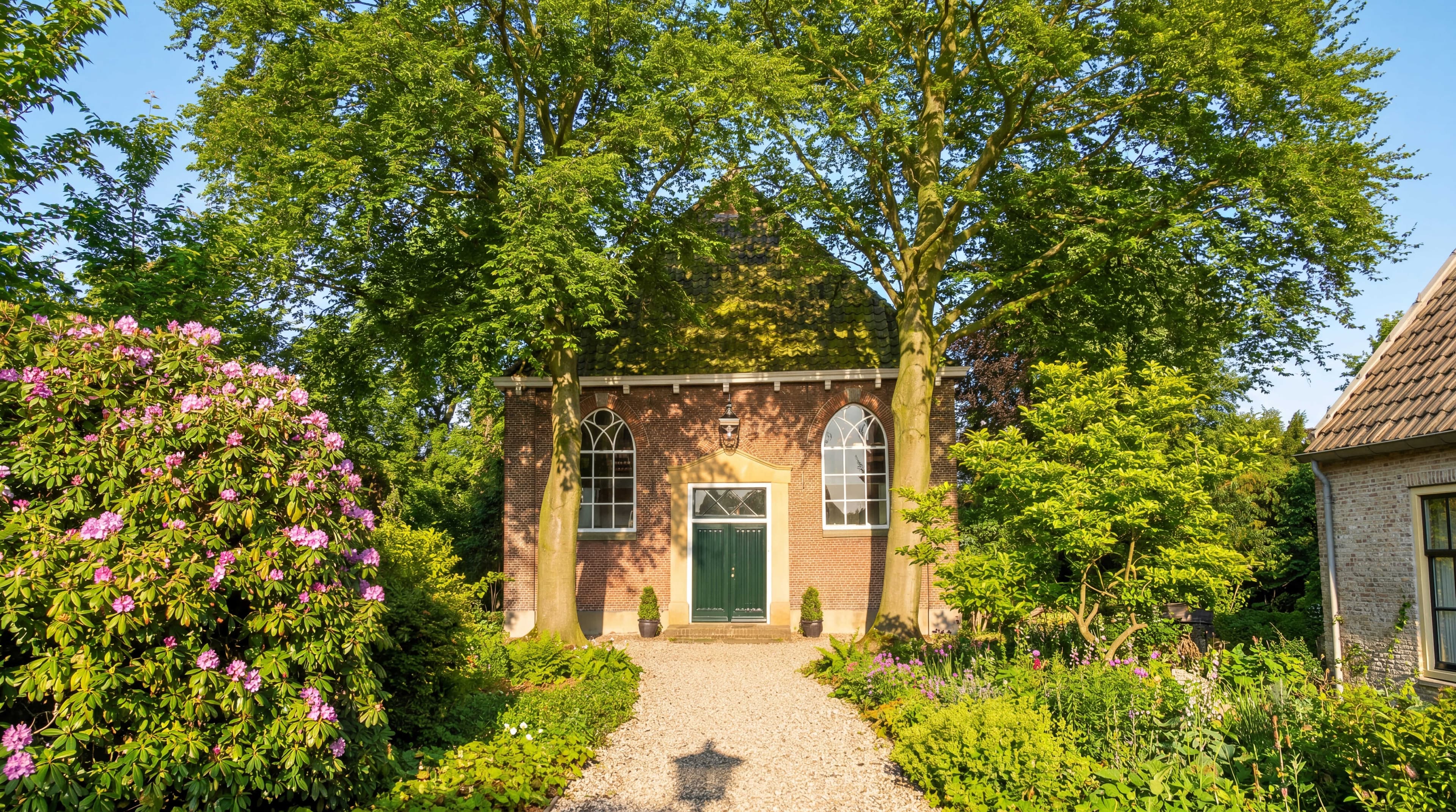 Remonstrantse kerk Nieuwkoop: bakstenen gevel met groene deuren, omringd door tuin en bloeiende rododendrons